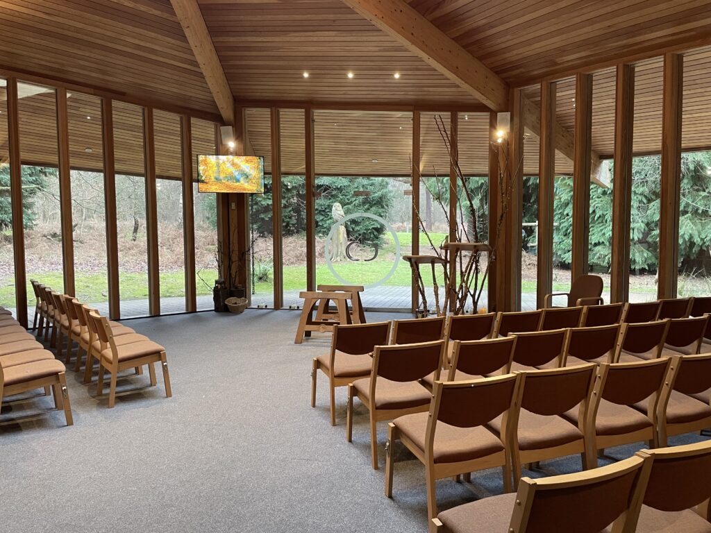 Inside of Greenacres Epping Park Woodland Hall with chairs set in front of a glass wall looking out into woodland